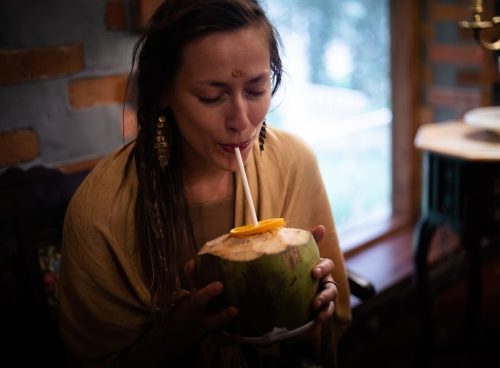 Woman enjoying fresh coconut water with a slice of orange, practicing Ayurvedic hydration at a wellness retreat.