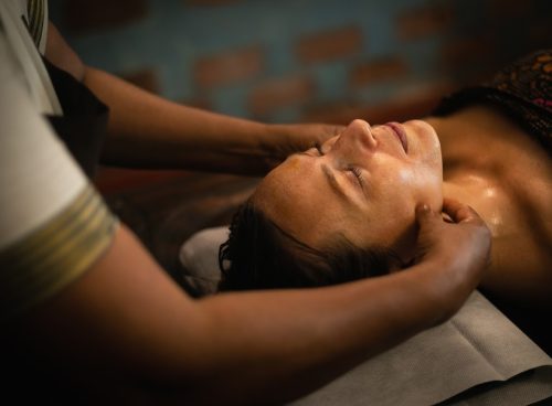 Woman receiving traditional Ayurvedic facial massage with herbal oil at Kairali Ayurvedic Healing Village in Kerala
