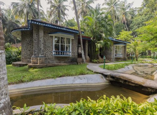 Traditional stone cottage at Kairali – The Ayurvedic Healing Village surrounded by tropical greenery and water canal in Kerala.