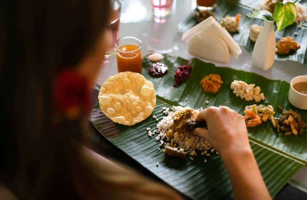 Person eating traditional South Indian Ayurvedic meal served on a banana leaf with rice, curries, vegetables, and papad at a wellness retreat