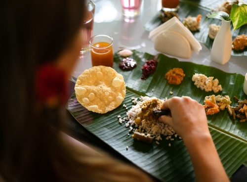 Person eating traditional South Indian Ayurvedic meal served on a banana leaf with rice, curries, vegetables, and papad at a wellness retreat
