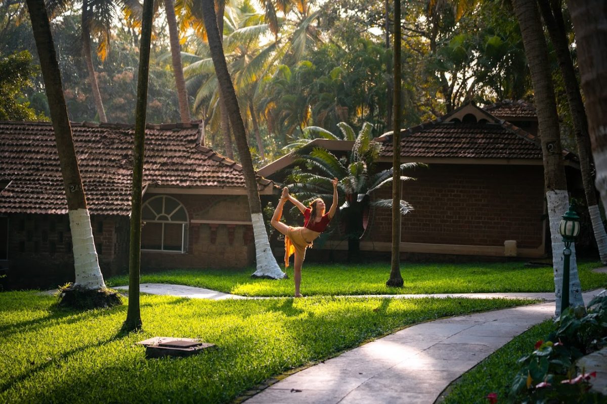 Current image: Woman practicing yoga outdoors at Kairali Ayurvedic Health Village in Kerala, surrounded by lush greenery and traditional cottages.