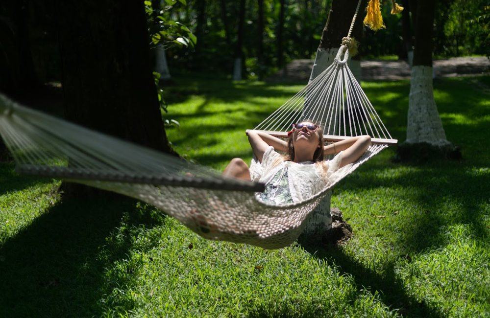 Woman relaxing on a hammock under the shade of trees at Kairali – The Ayurvedic Healing Village in Kerala.