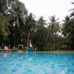 Woman practicing yoga near a serene pool surrounded by tropical palm trees at an Ayurvedic retreat in Kerala.