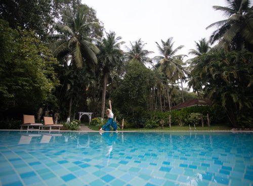 Woman practicing yoga near a serene pool surrounded by tropical palm trees at an Ayurvedic retreat in Kerala.