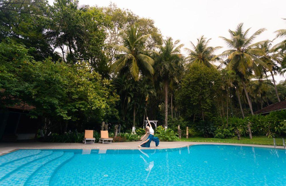 Woman practicing yoga beside a pool at Kairali Ayurvedic Health Village surrounded by lush palm trees and greenery in Kerala, India