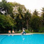 Woman practicing yoga beside a pool at Kairali Ayurvedic Health Village surrounded by lush palm trees and greenery in Kerala, India