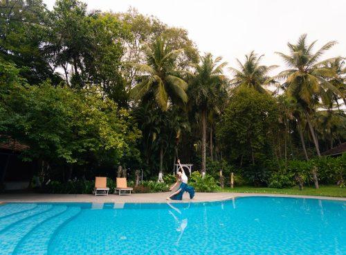 Woman practicing yoga beside a pool at Kairali Ayurvedic Health Village surrounded by lush palm trees and greenery in Kerala, India