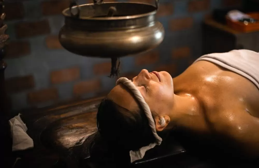 Woman receiving traditional Ayurvedic Shirodhara therapy with warm herbal oil gently poured on the forehead.