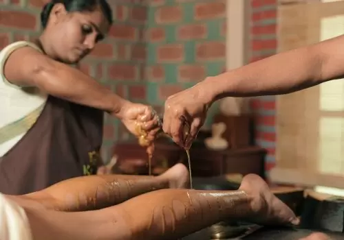 Two Ayurvedic therapists performing traditional oil therapy on a patient’s legs using warm herbal oils at Kairali Ayurvedic Health Retreat in Palakkad, Kerala.