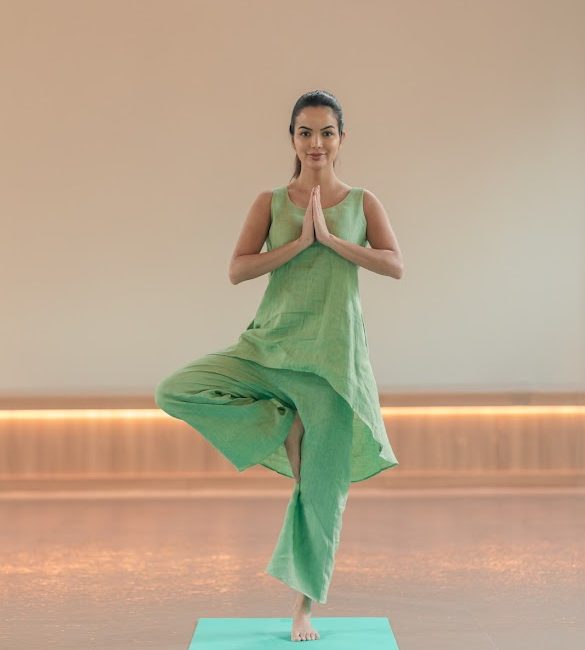 Woman practicing tree pose (Vrikshasana) on yoga mat at Ayurvedic wellness center in Kerala