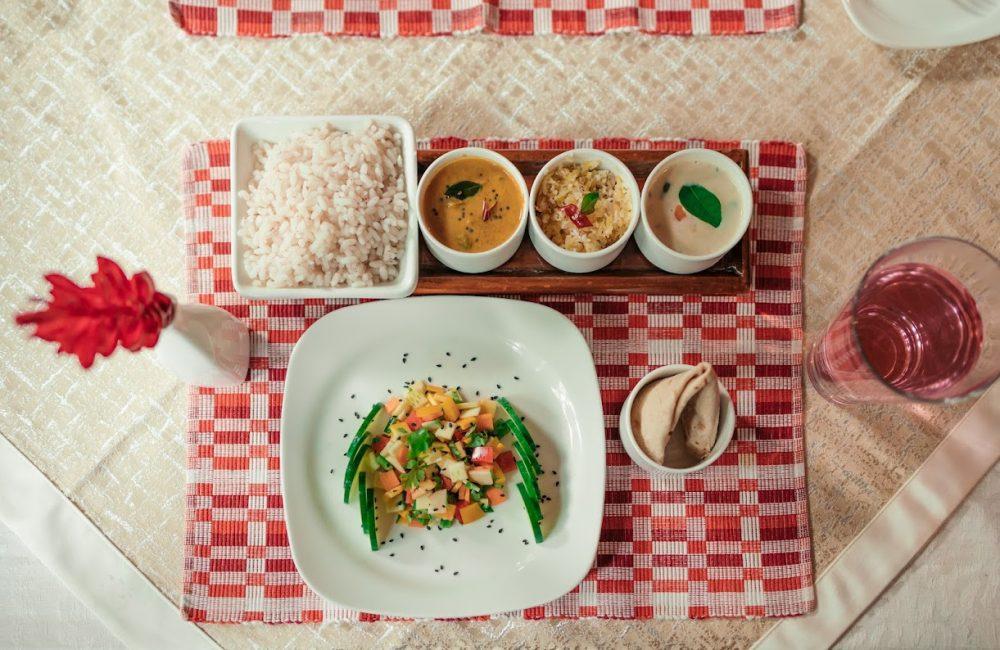Ayurvedic thali meal at Kairali Ayurvedic Health Village with red rice, curry, vegetable dishes, salad, papad, and herbal water on a traditional setting.