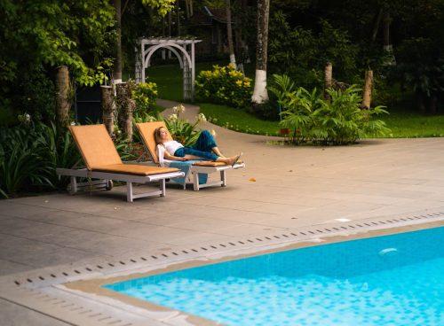 Woman relaxing by the poolside at Kairali Ayurvedic Healing Village surrounded by lush greenery in Kerala