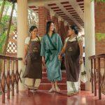 Solo female guest being warmly welcomed by two Kairali Ayurvedic therapists at the Healing Village in Kerala
