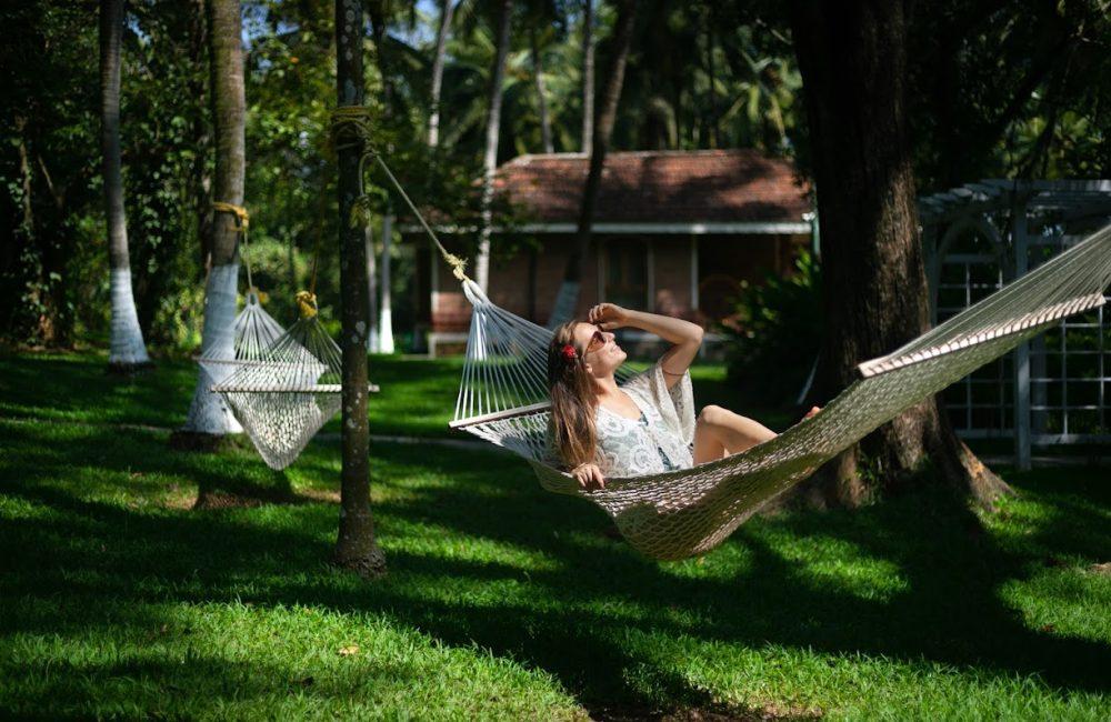 Solo female traveler relaxing on a hammock beneath palm trees at Kairali – The Ayurvedic Healing Village, Kerala, India.
