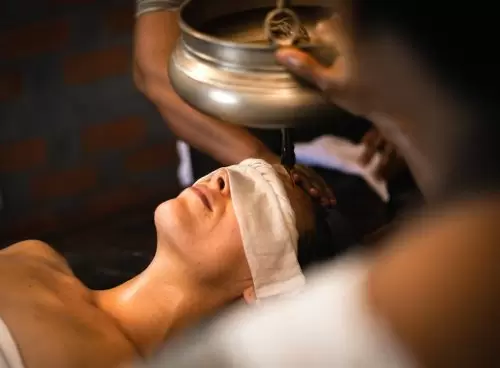 Close-up of a woman receiving Shirodhara therapy—warm herbal oil streaming onto the forehead—at Kairali – The Ayurvedic Healing Village, Kerala.