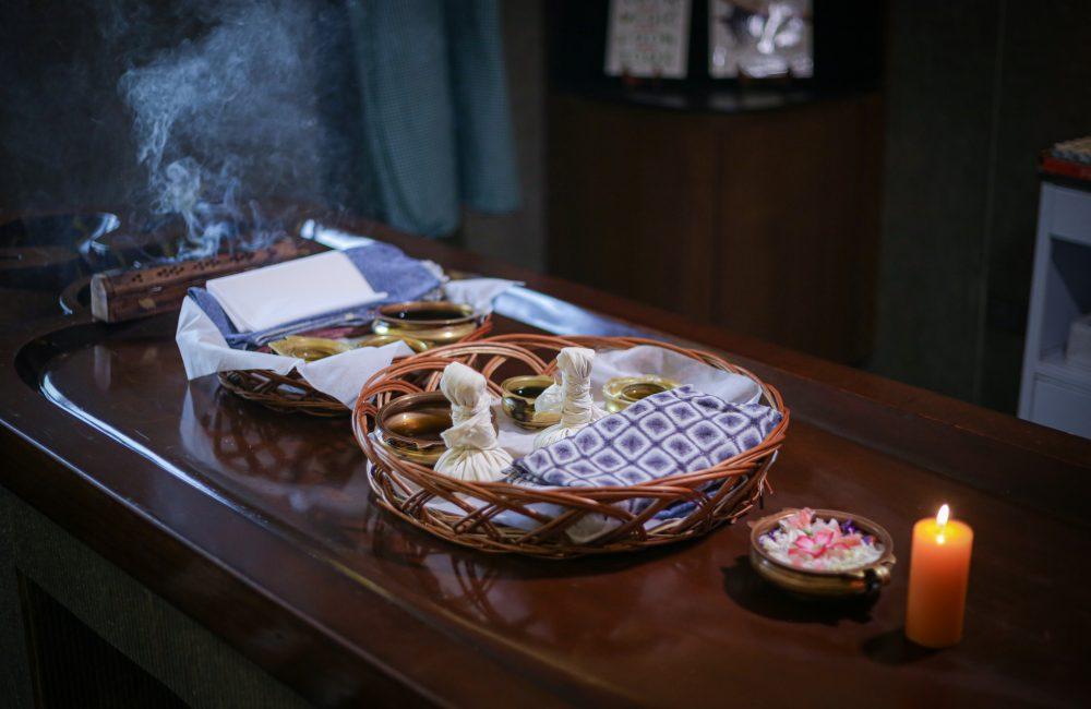 Ayurvedic therapy setup with warm herbal oils, linen potli compresses, incense smoke and candle at Kairali – The Ayurvedic Healing Village