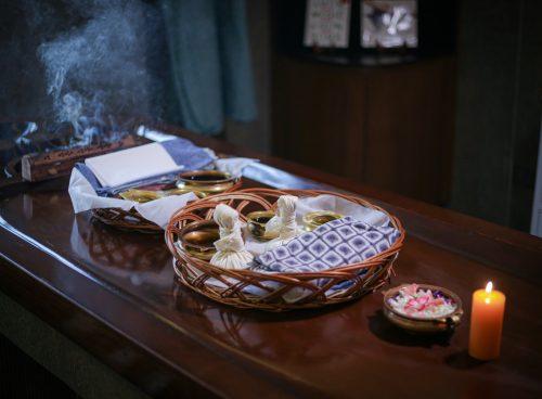 Ayurvedic therapy setup with warm herbal oils, linen potli compresses, incense smoke and candle at Kairali – The Ayurvedic Healing Village