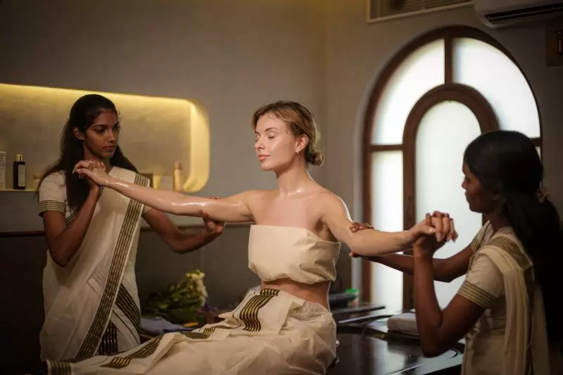 Woman receiving traditional Ayurvedic abhyanga oil therapy from two female therapists in a serene Kerala retreat centre.