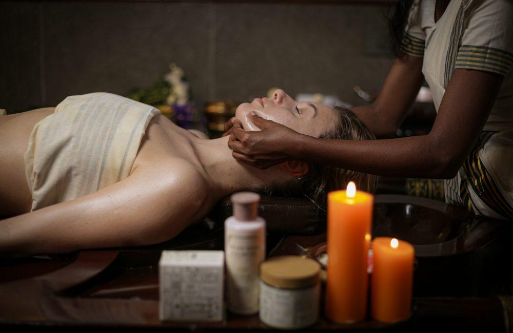 Ayurvedic facial massage at Kairali – therapist massaging a guest’s face beside warm candlelight in a traditional Kerala treatment room