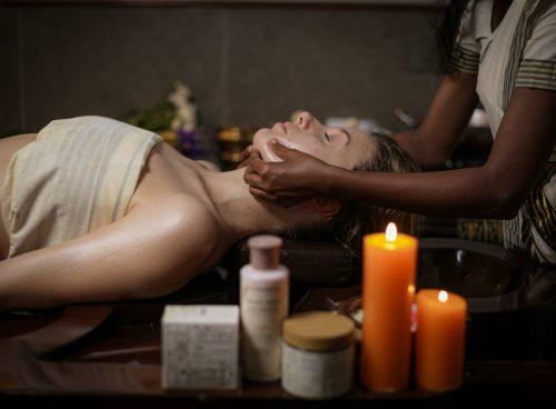 Ayurvedic facial massage at Kairali – therapist massaging a guest’s face beside warm candlelight in a traditional Kerala treatment room