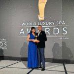 Award ceremony photo: Kairali representative receiving a World Luxury Spa Awards trophy on stage, against the event backdrop.