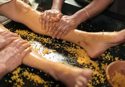 Ayurvedic herbal scrub (ubtan) leg massage by female therapists at a Kerala retreat, with warm oil and turmeric blend—authentic, women-first care.
