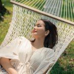 Relaxed solo female traveler resting on a hammock in lush greenery at a Kerala wellness retreat.