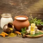 Earthen pot of milk, brass cup pouring ghee, and paneer cubes with spices—Ayurvedic dairy setup at a Kerala wellness retreat.