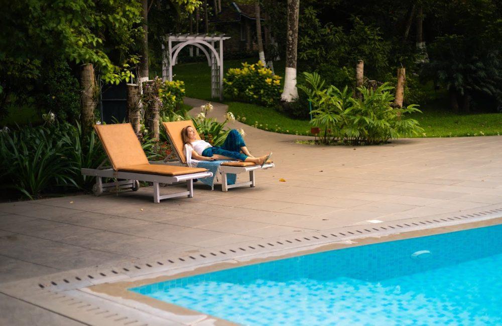 Solo female guest relaxing on a poolside lounger amid lush gardens at Kairali retreat Kerala—a calm, safe setting for authentic Ayurveda and yoga.