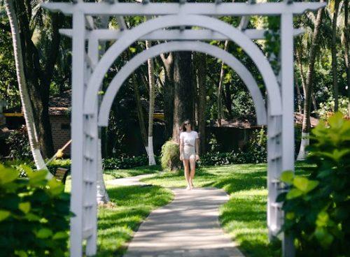 Solo woman walking along a curved garden path under a white arch at Kairali – The Ayurvedic Healing Village, Palakkad.
