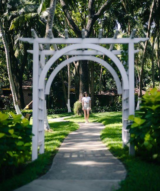 Solo woman walking along a curved garden path under a white arch at Kairali – The Ayurvedic Healing Village, Palakkad.
