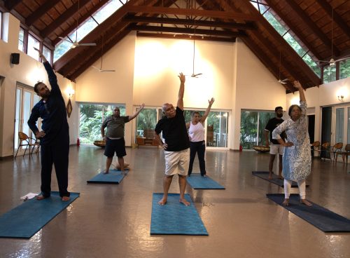 Senior guests practicing gentle side-bend yoga on mats in a spacious, well-lit hall at Kairali Ayurvedic Health Village Kerala—an accessible ayurvedic retreat Kerala.
