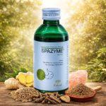 Green bottle of Kairali Spazyme Syrup (200 ml) placed outdoors on a wooden surface, surrounded by fennel seeds, long pepper, ginger, rock salt, and a bowl of ground herbs, representing natural digestive care.