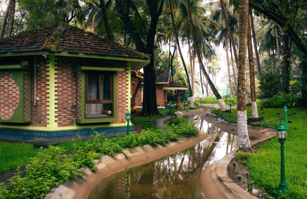 Traditional brick cottage beside a palm-lined waterway after rain at Kairali Ayurvedic Palakkad, Kerala—a tranquil wellness retreat setting.
