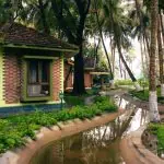 Traditional brick cottage beside a palm-lined waterway after rain at Kairali Ayurvedic Palakkad, Kerala—a tranquil wellness retreat setting.
