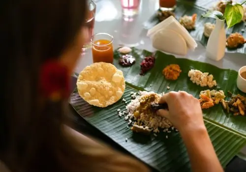 Guest enjoying a Kerala banana-leaf meal—rice, dal, papad and seasonal veg sides—at Kairali Ayurvedic Healing Village.