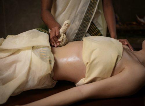 Ayurvedic abdominal therapy with a warm herbal compress (kizhi) during oil massage at Kairali Ayurvedic Healing Village, Palakkad, Kerala.