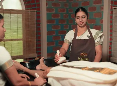 Female Ayurvedic therapists performing kizhi (herbal poultice) treatment on a guest at Kairali – The Ayurvedic Healing Village, Kerala.