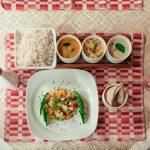 Ayurvedic thali | Kerala red rice | Ayurveda Aahara traditional diet | sattvic meal with vegetable curries, cucumber salad, black sesame, and pink herbal drink on red-white placemat | FSSAI Ayurveda Aahara compliant presentation