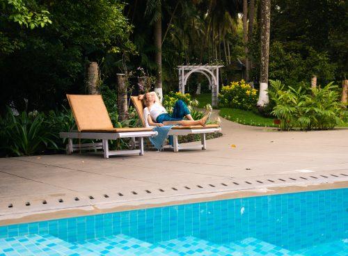 Guest relaxing on a sun lounger beside a blue-tiled pool surrounded by lush tropical greenery.