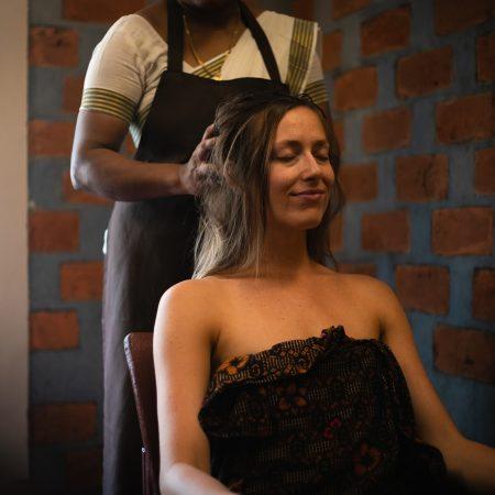 Ayurvedic therapist gently massages a woman’s scalp as she sits relaxed with eyes closed in a serene treatment room.