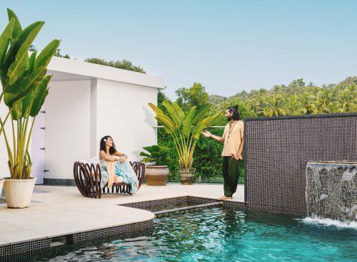 Couple relaxing by the infinity pool at Villa Raag in South Goa, surrounded by tropical greenery and a waterfall feature.