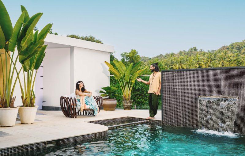 Couple relaxing by the infinity pool at Villa Raag in South Goa, surrounded by tropical greenery and a waterfall feature.
