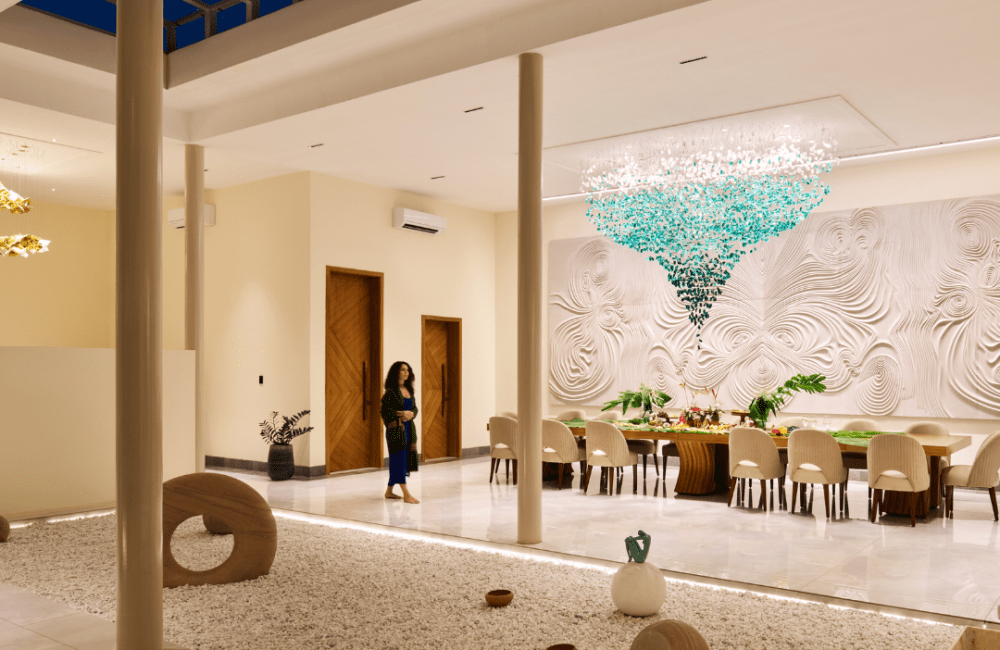 Open-to-sky dining pavilion at Villa Raag with a long table, teal chandelier, sculptural wall art, and a zen gravel court.