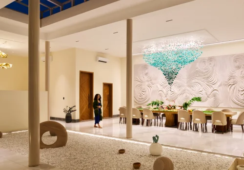 Open-to-sky dining pavilion at Villa Raag with a long table, teal chandelier, sculptural wall art, and a zen gravel court.