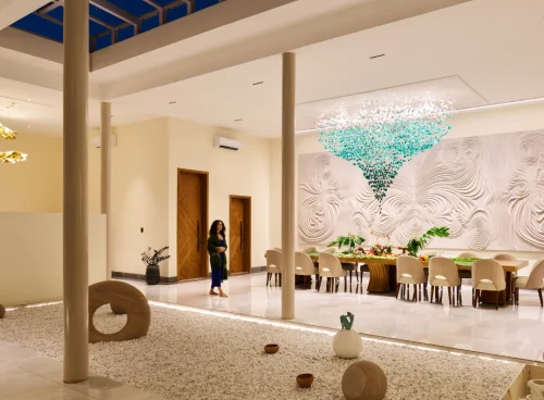 Open-to-sky dining pavilion at Villa Raag with a long table, teal chandelier, sculptural wall art, and a zen gravel court.