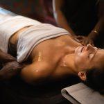 Woman receiving a traditional Ayurvedic four-hand massage at a spa, lying on a massage table with eyes closed