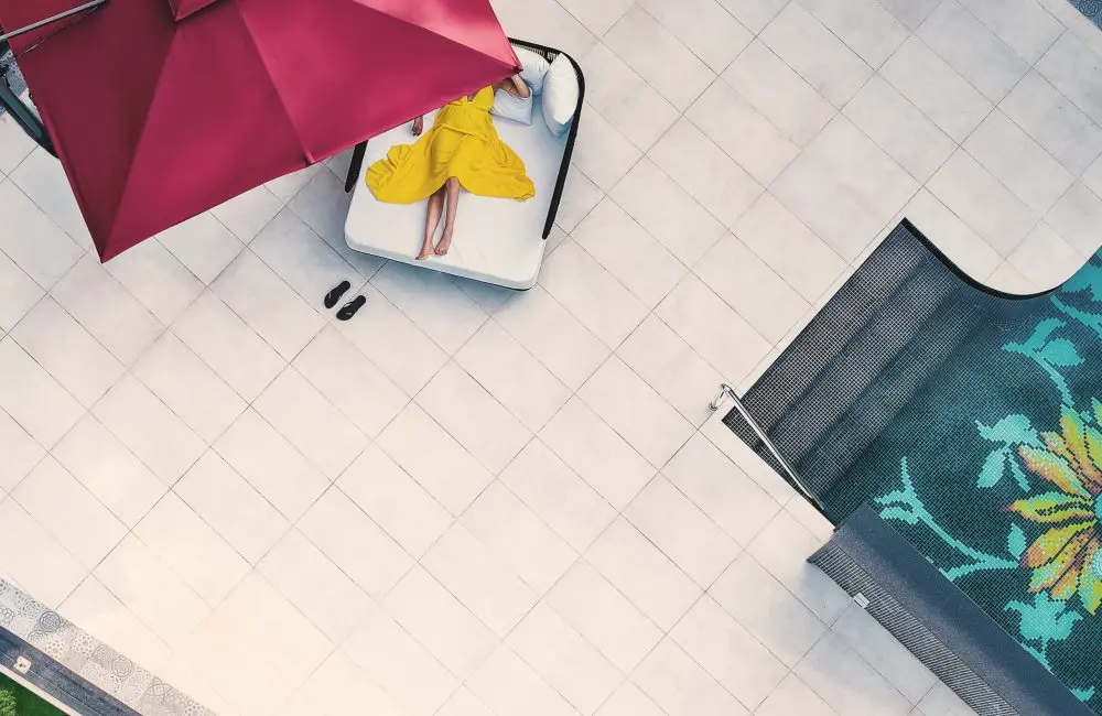 Aerial view of a guest relaxing on a sun lounger under a red umbrella beside a patterned pool at Villa Raag.