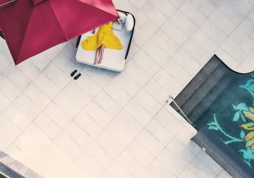 Aerial view of a guest relaxing on a sun lounger under a red umbrella beside a patterned pool at Villa Raag.